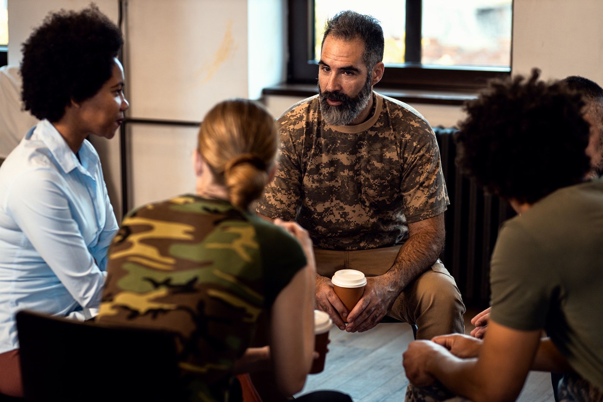 Group of diverse veterans talking during PTSD support group.