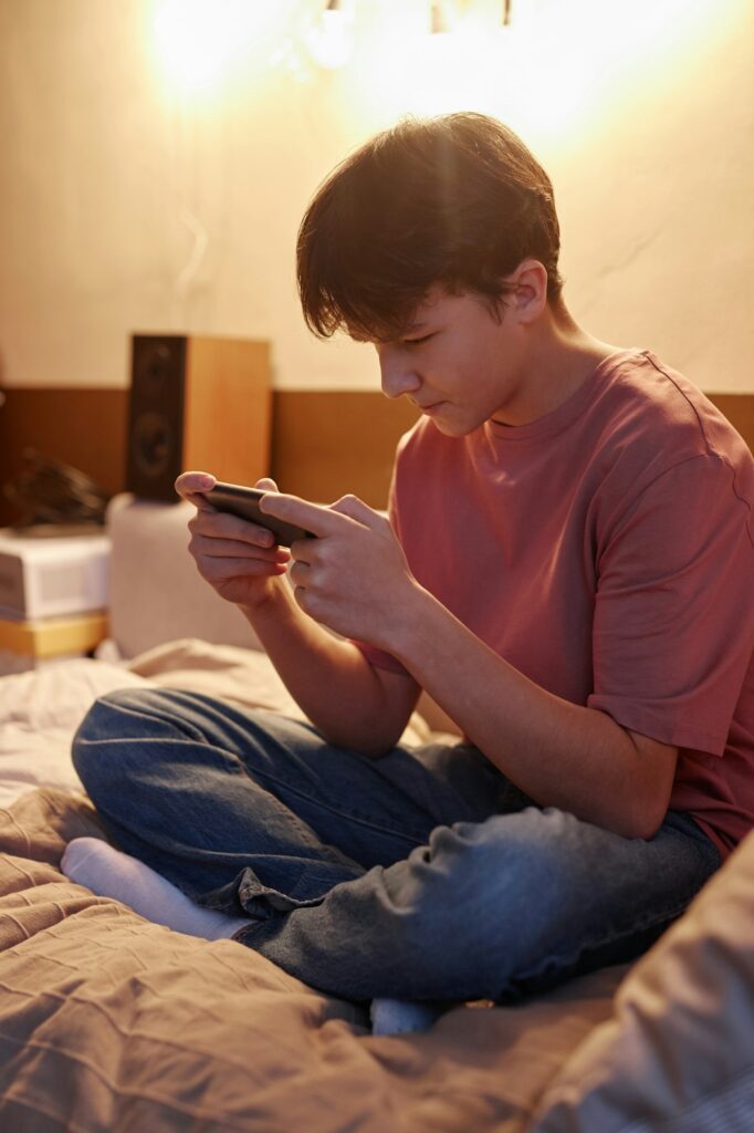 Teen Boy Playing Mobile Games Sitting on Bed