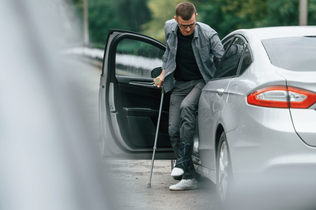Injured man with crutches is going out from the car